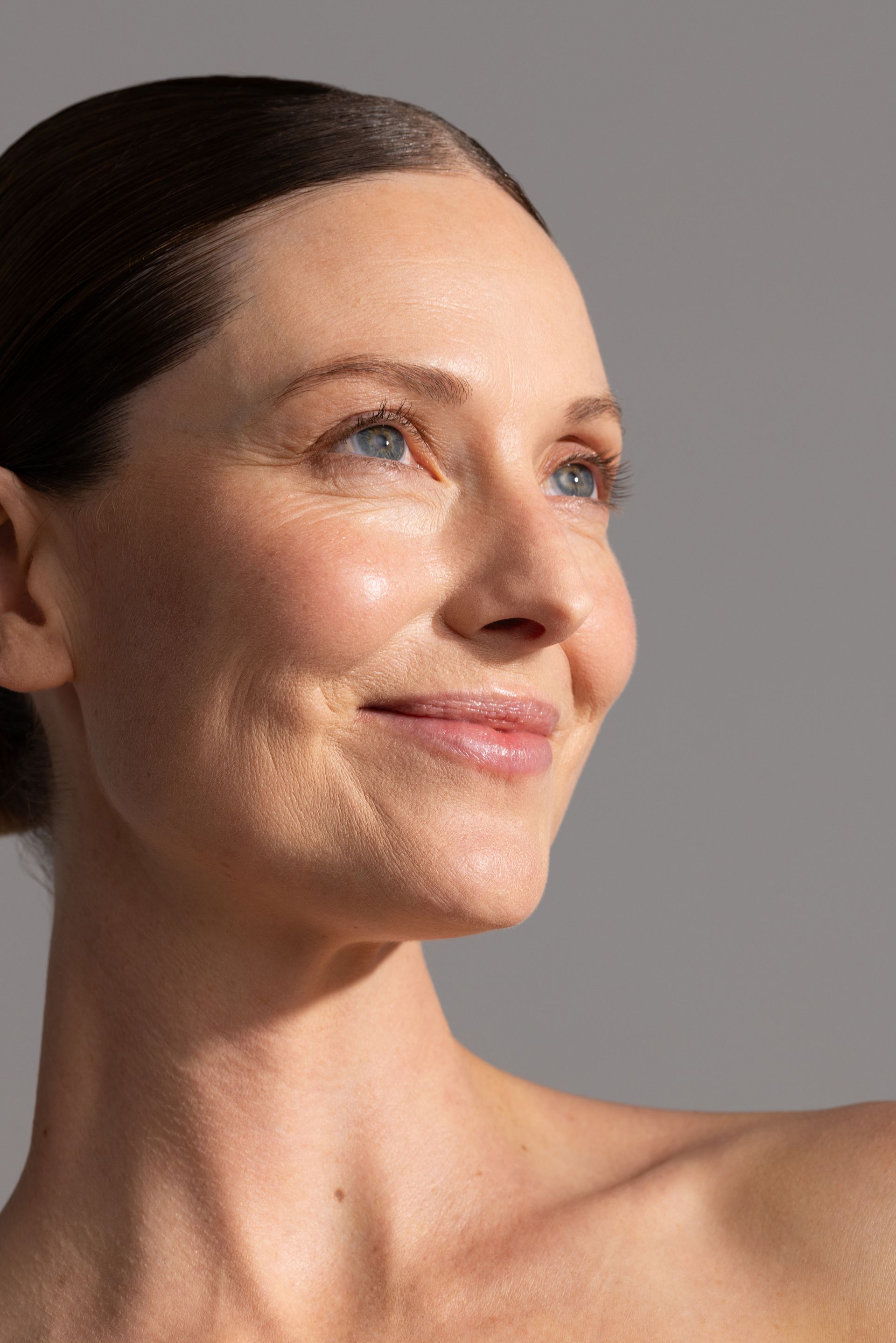 A side profile of a person with a neutral expression and light skin, looking away against a soft gray background — Skin Haven Aesthetics Whitsundays in Airlie Beach, QLD