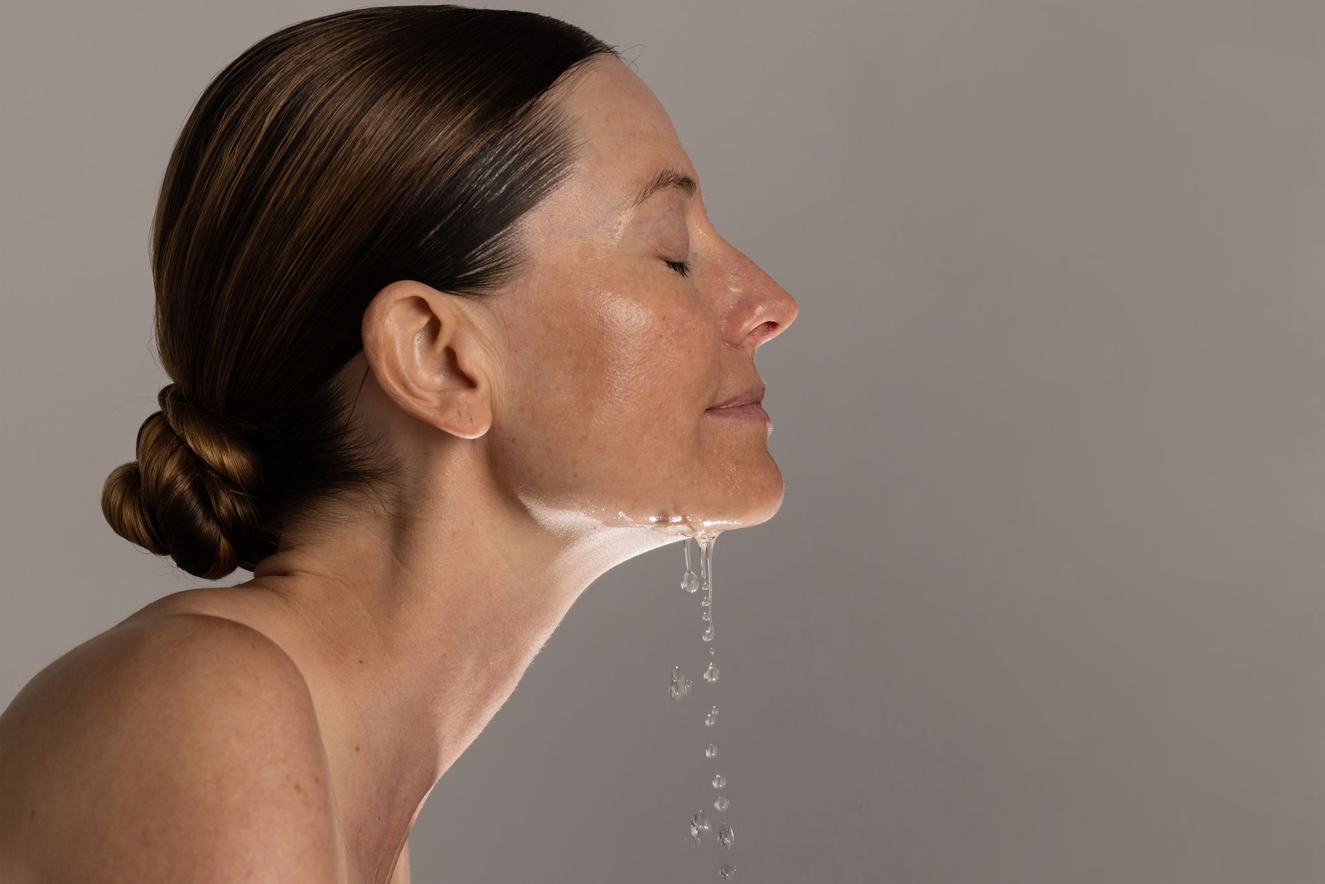 A person with hair pulled back in a bun splashes water on their face, with droplets falling from their chin — Skin Haven Aesthetics Whitsundays in Airlie Beach, QLD