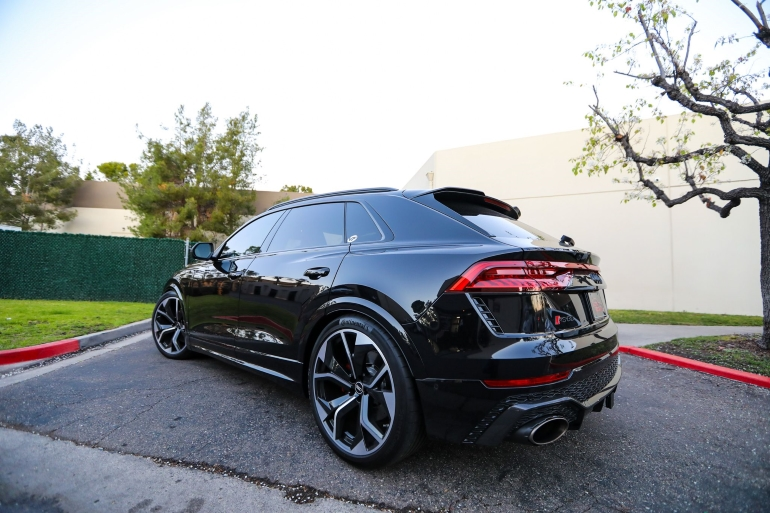 Black SUV parked on a street with tinted windows and large alloy wheelsSilver and neon yellow sports car with oversized rear wing parked beside a white wall. | Pacific German