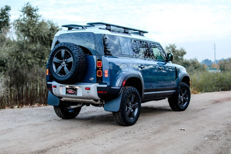 Blue off-road SUV parked on a dirt road beside trees, rear view with spare tire visibleSilver and neon yellow sports car with oversized rear wing parked beside a white wall. | Pacific German