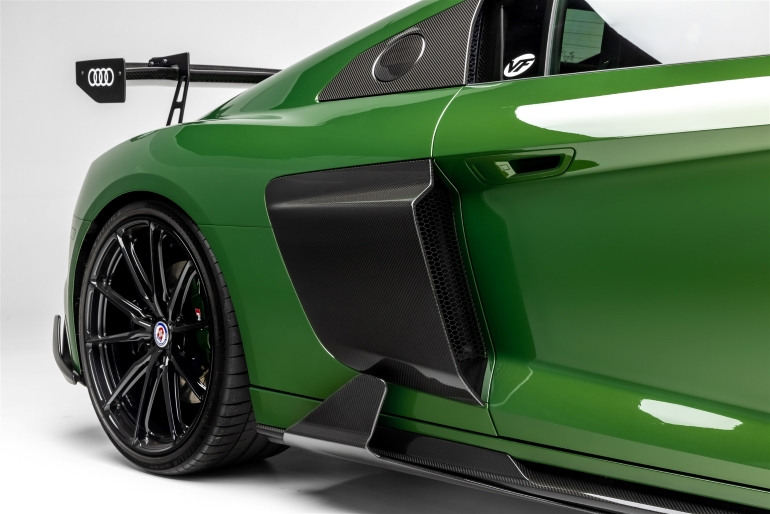 Close-up of a green sports car’s rear side with black wheel, spoiler, and side ventSilver and neon yellow sports car with oversized rear wing parked beside a white wall. | Pacific German