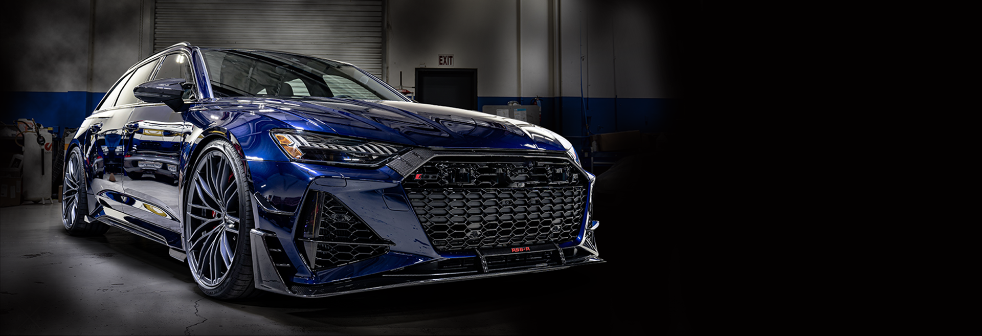 Blue sports sedan in a dark studio, front three-quarter view with a large mesh grille and silver wheels | Pacific German