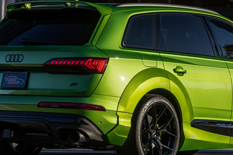 Bright green Audi SUV viewed from the rear at a car show with black wheels and tinted windowsSilver and neon yellow sports car with oversized rear wing parked beside a white wall. | Pacific German