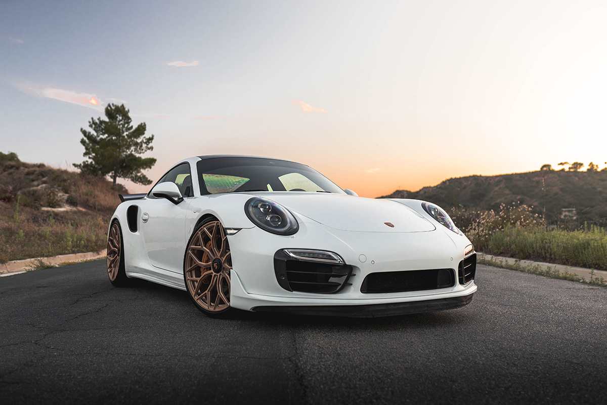 White sports car parked on a road at sunset, with a countryside hillside in the backgroundSilver and neon yellow sports car with oversized rear wing parked beside a white wall. | Pacific German