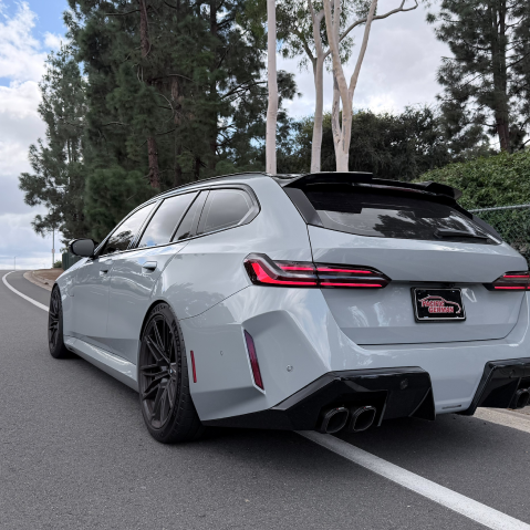 Modified gray station wagon on a curving road, rear view with black rims and quad exhaust | Pacific Germany