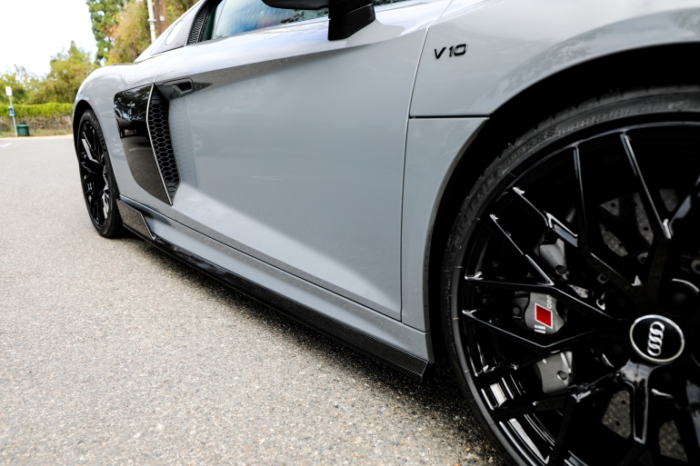 Silver sports car with black rims parked on pavement, side view close-upSilver and neon yellow sports car with oversized rear wing parked beside a white wall. | Pacific German