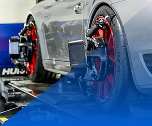 Silver sports car on a chassis dyno with red wheels in a garage, viewed from the rear side | Pacific German