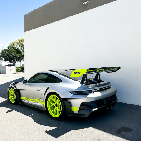 Silver and neon yellow sports car with oversized rear wing parked beside a white wall. | Pacific German