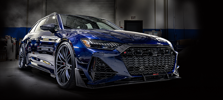 Blue sports sedan in a dark studio, front three-quarter view with a large mesh grille and silver wheels | Pacific German