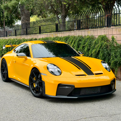 Yellow sports car with black racing stripes parked on a street beside a hedge and fence | Pacific Germany