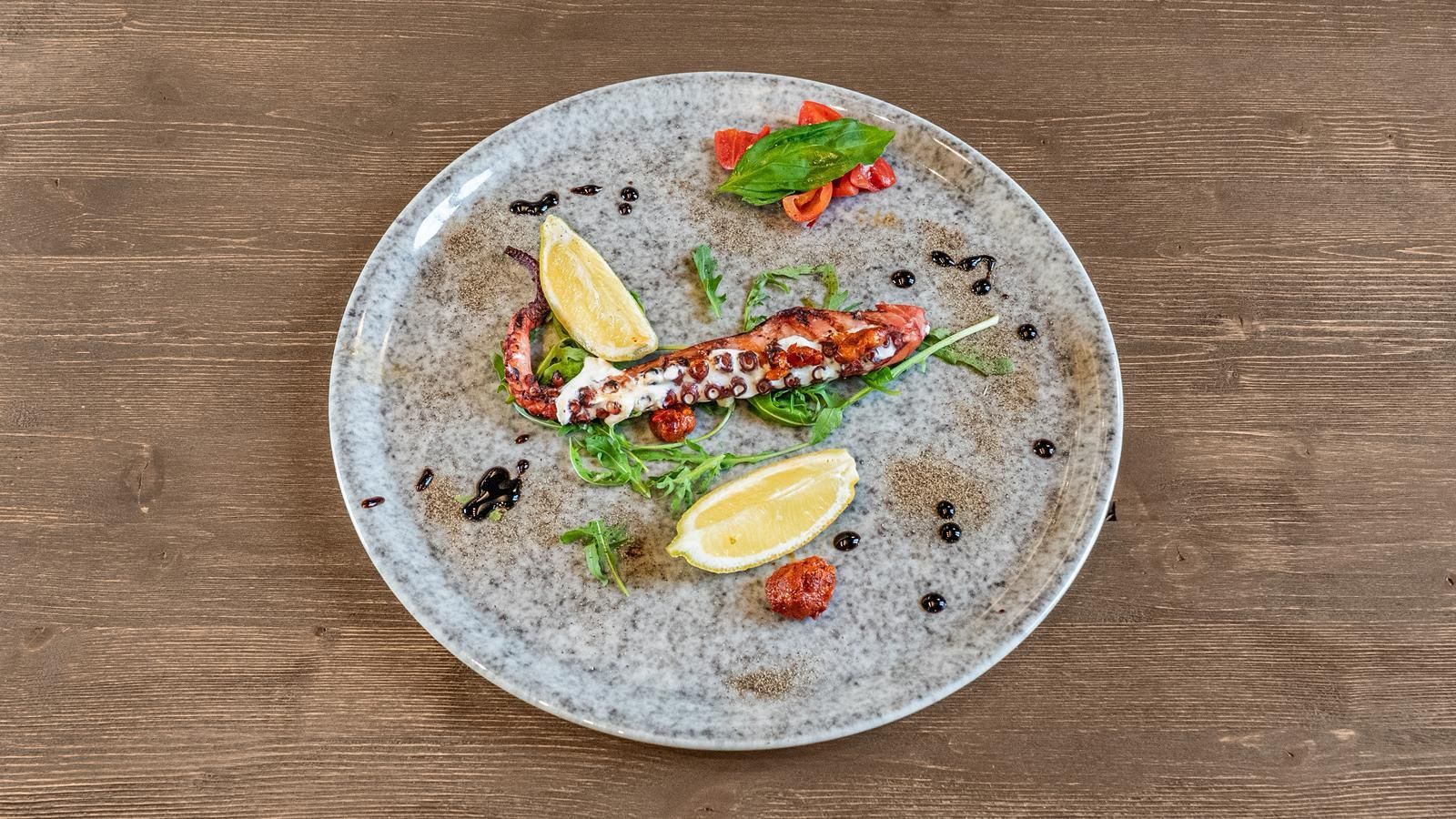 Pesce alla griglia su un piatto grigio, con spicchi di limone ed erbe aromatiche, su un tavolo di legno