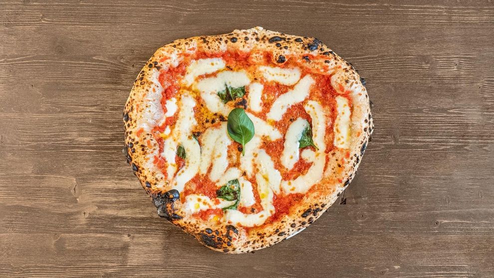 Pizza Margherita a forma di cuore su un tavolo di legno, con mozzarella e basilico.
