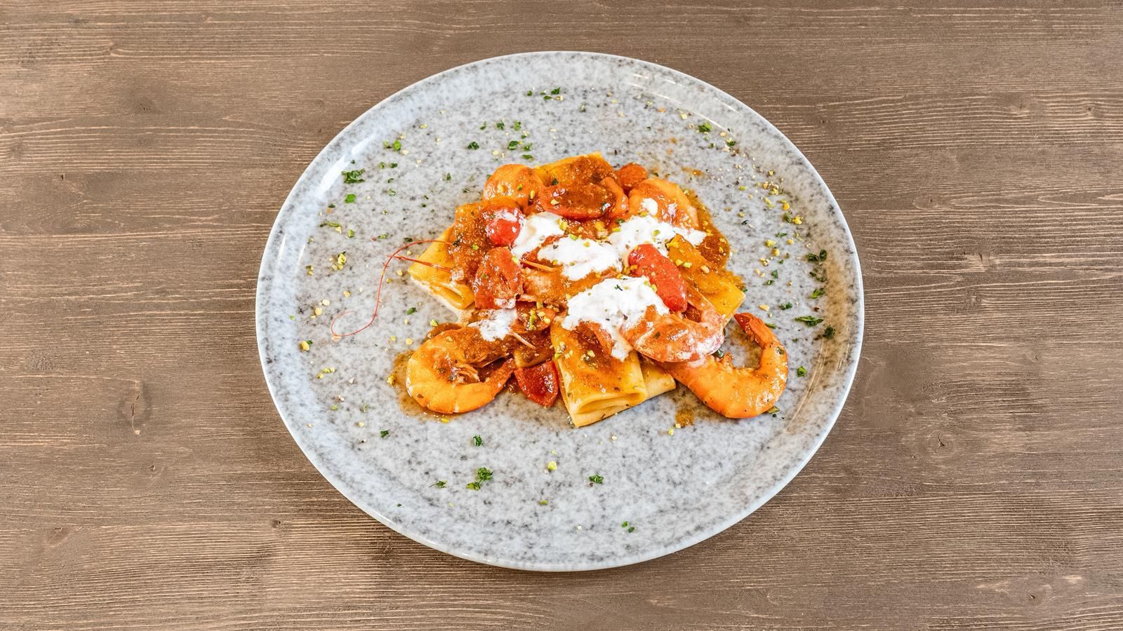 Piatto di pasta condito con salsa di pomodoro e formaggio, su un piatto grigio puntinato