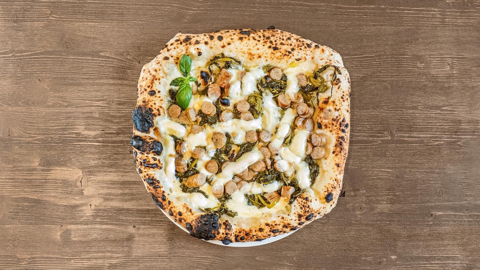 Pizza quadrata con formaggio fuso ed erbe aromatiche verdi su un tavolo di legno