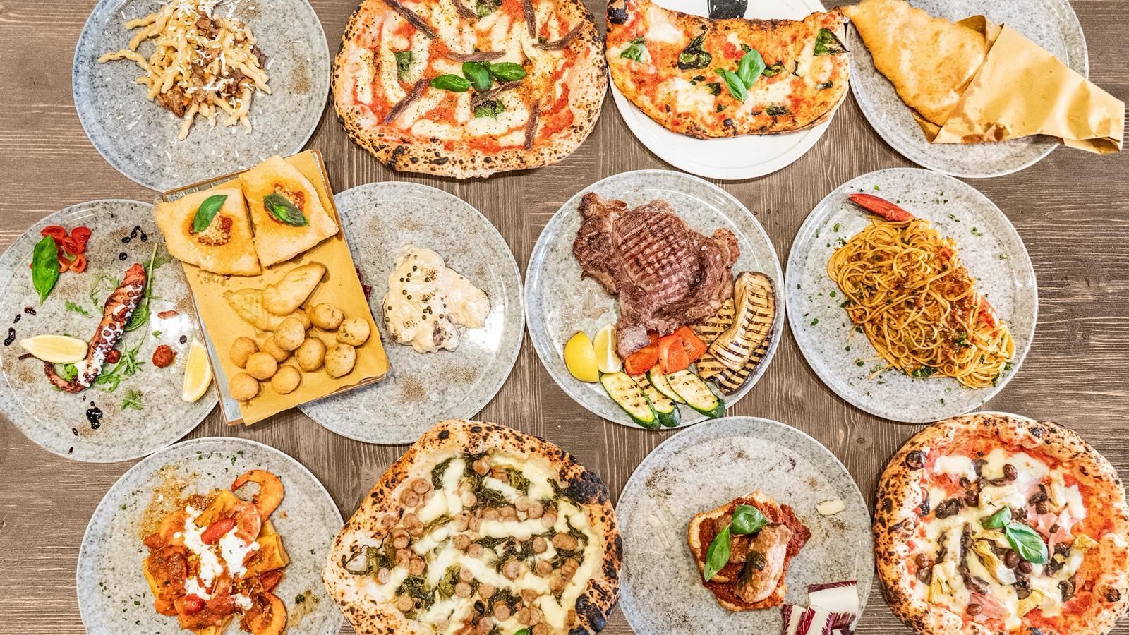 Pietanze assortite su un tavolo: pizza, carne alla griglia, riso, patatine fritte, insalata e pasticcini su piatti decorati.