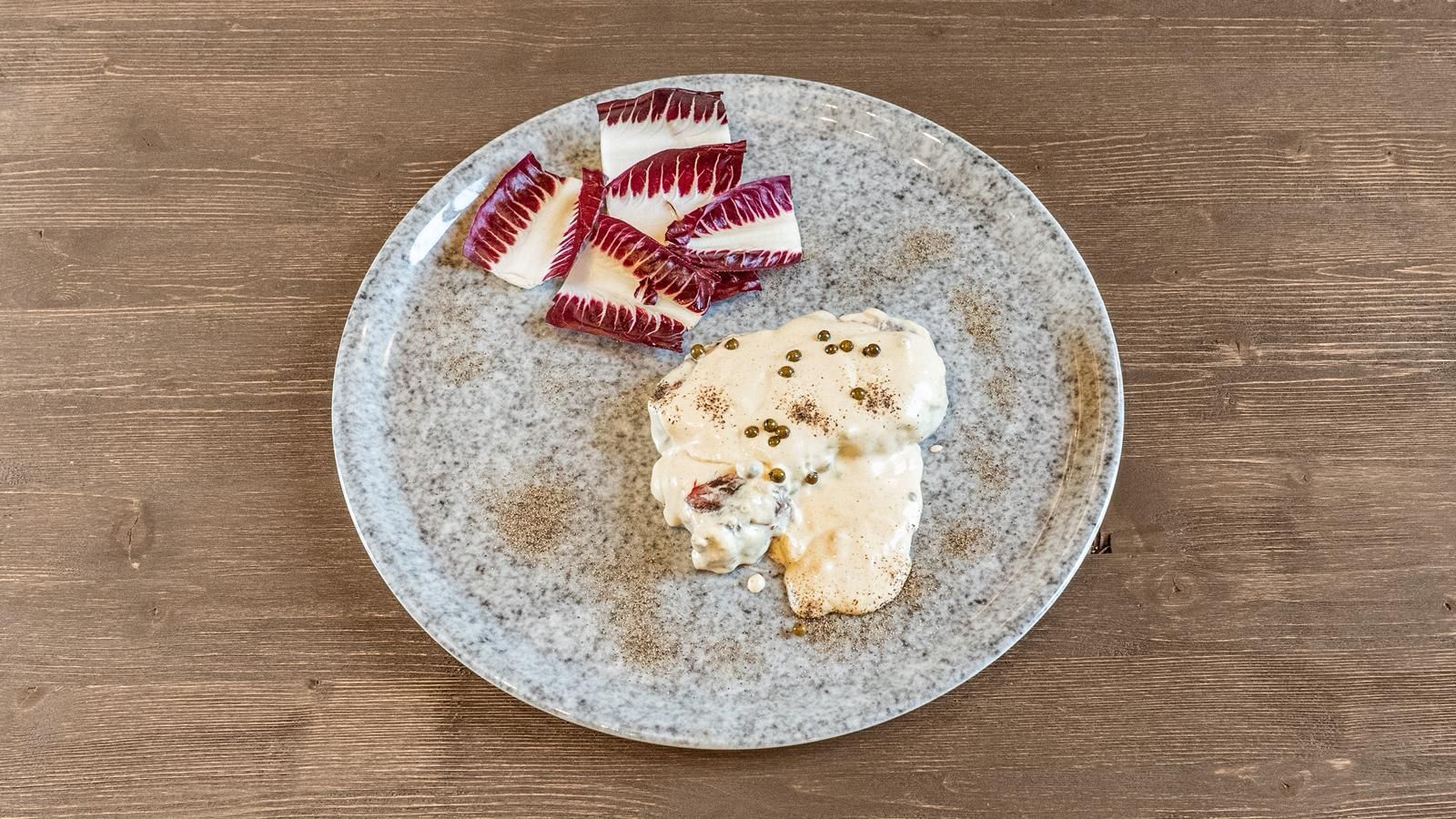 Piatto con frutta rossa a fette e una cucchiaiata di dessert cremoso cosparso di spezie su un tavolo di legno