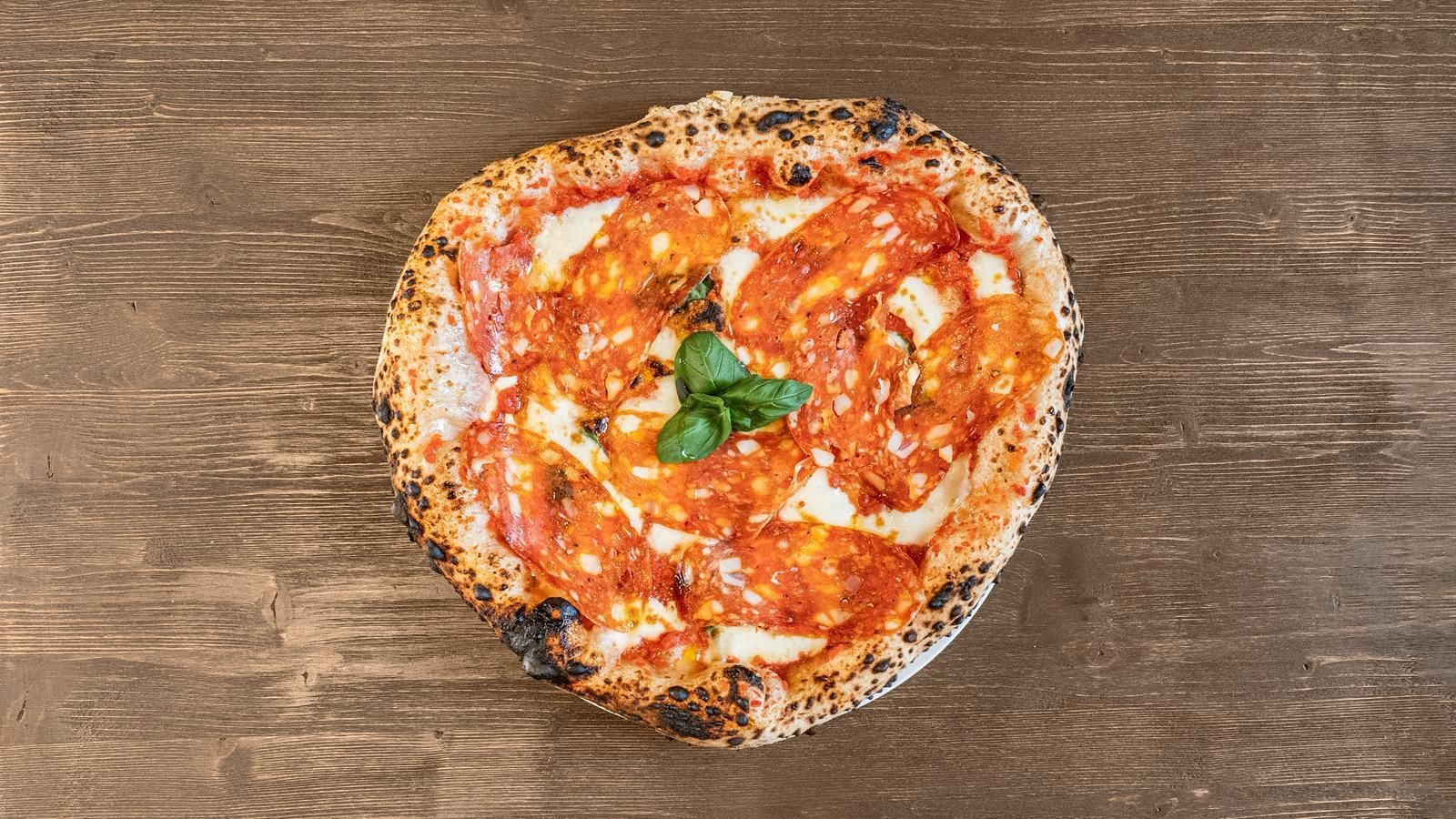 Pizza a forma di cuore con salsa di pomodoro, formaggio e basilico su un tavolo di legno.