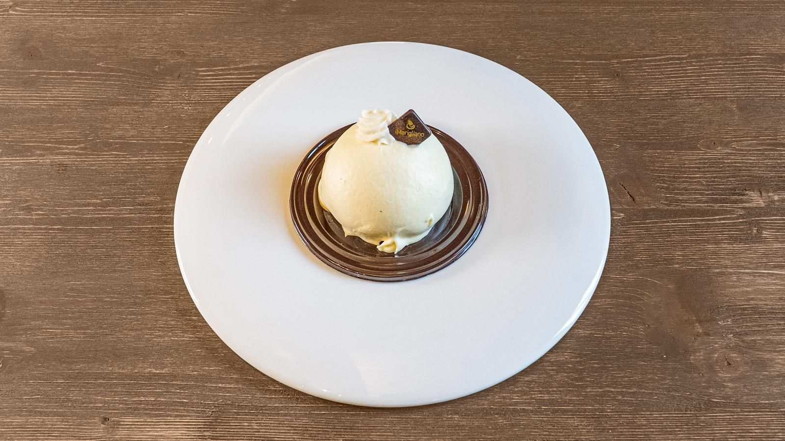 Dessert su un piatto bianco: una pallina di crema su un anello di cioccolato, su un tavolo di legno.