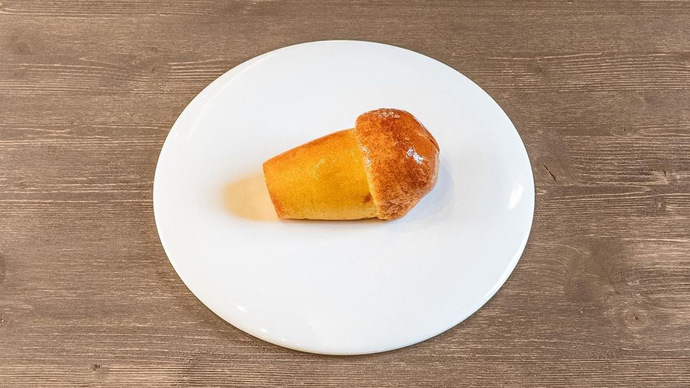 Piccolo pasticcino dorato su un piatto bianco, su un tavolo di legno.