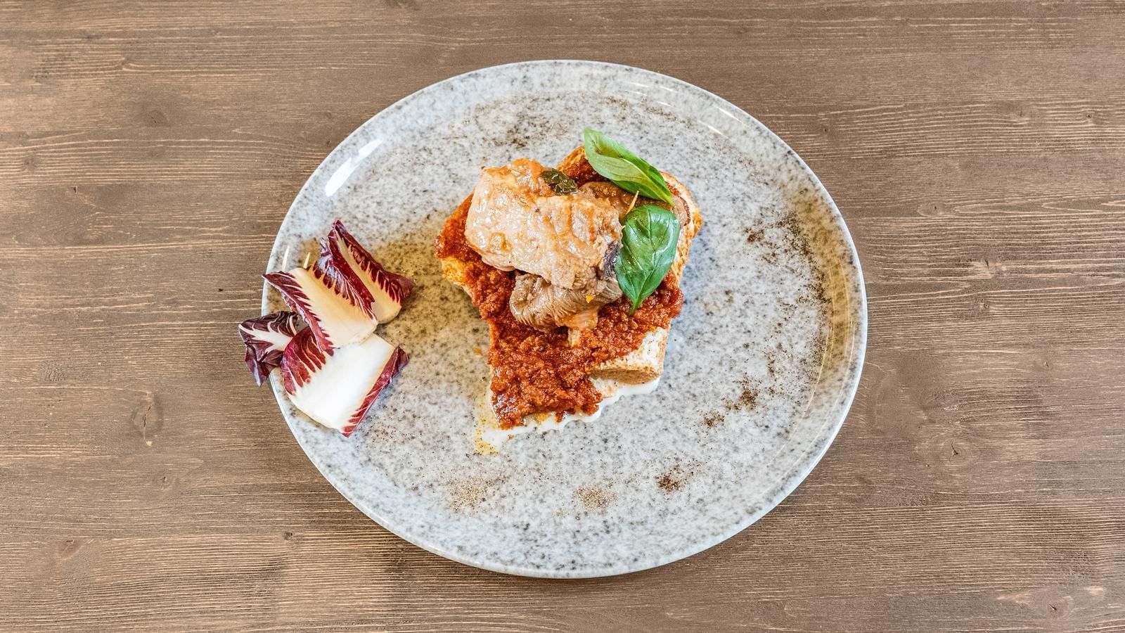 Piatto gourmet impiattato su un piatto grigio appoggiato su un tavolo di legno, con carne a fette e una guarnizione verde
