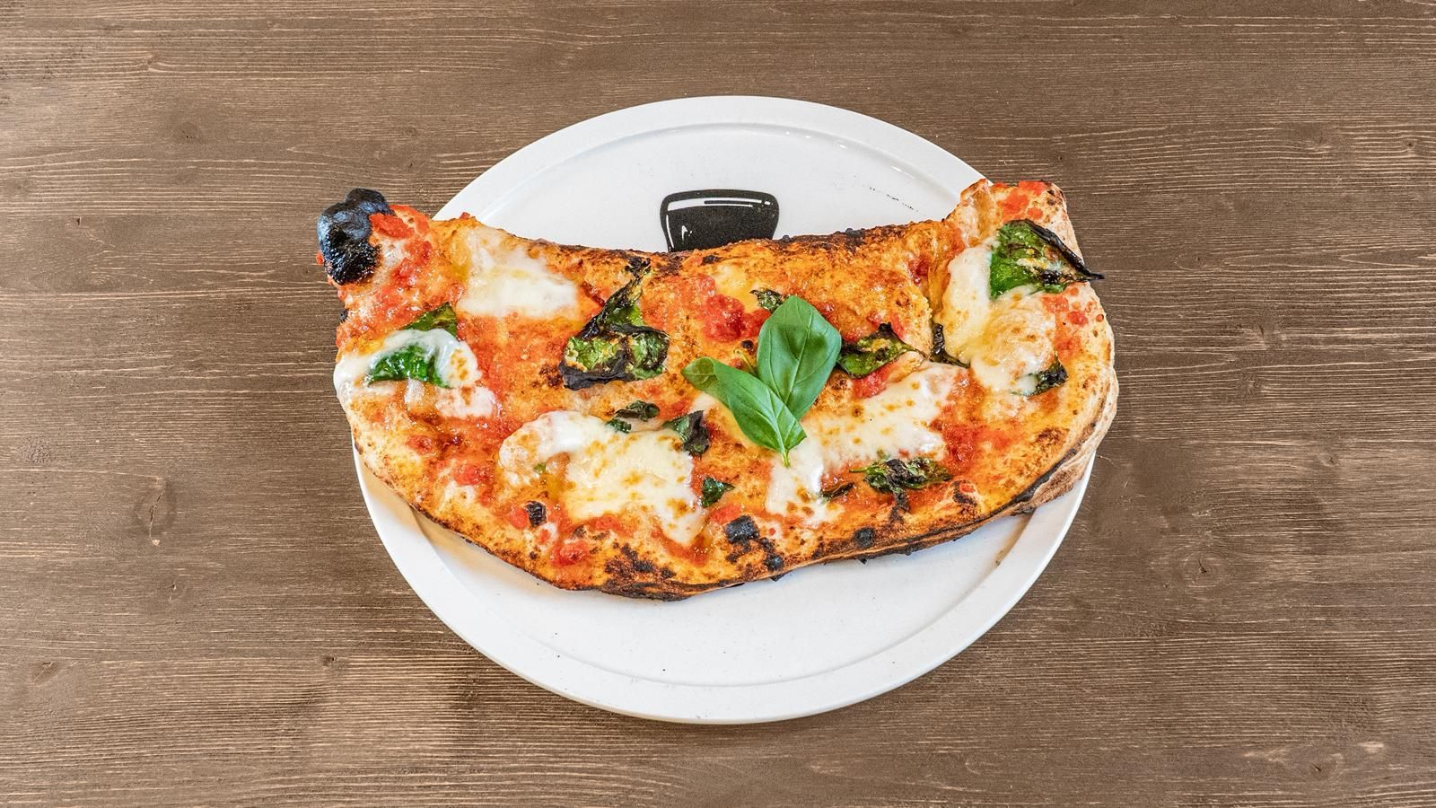 Pizza a fette con basilico su un piatto bianco sopra un tavolo di legno