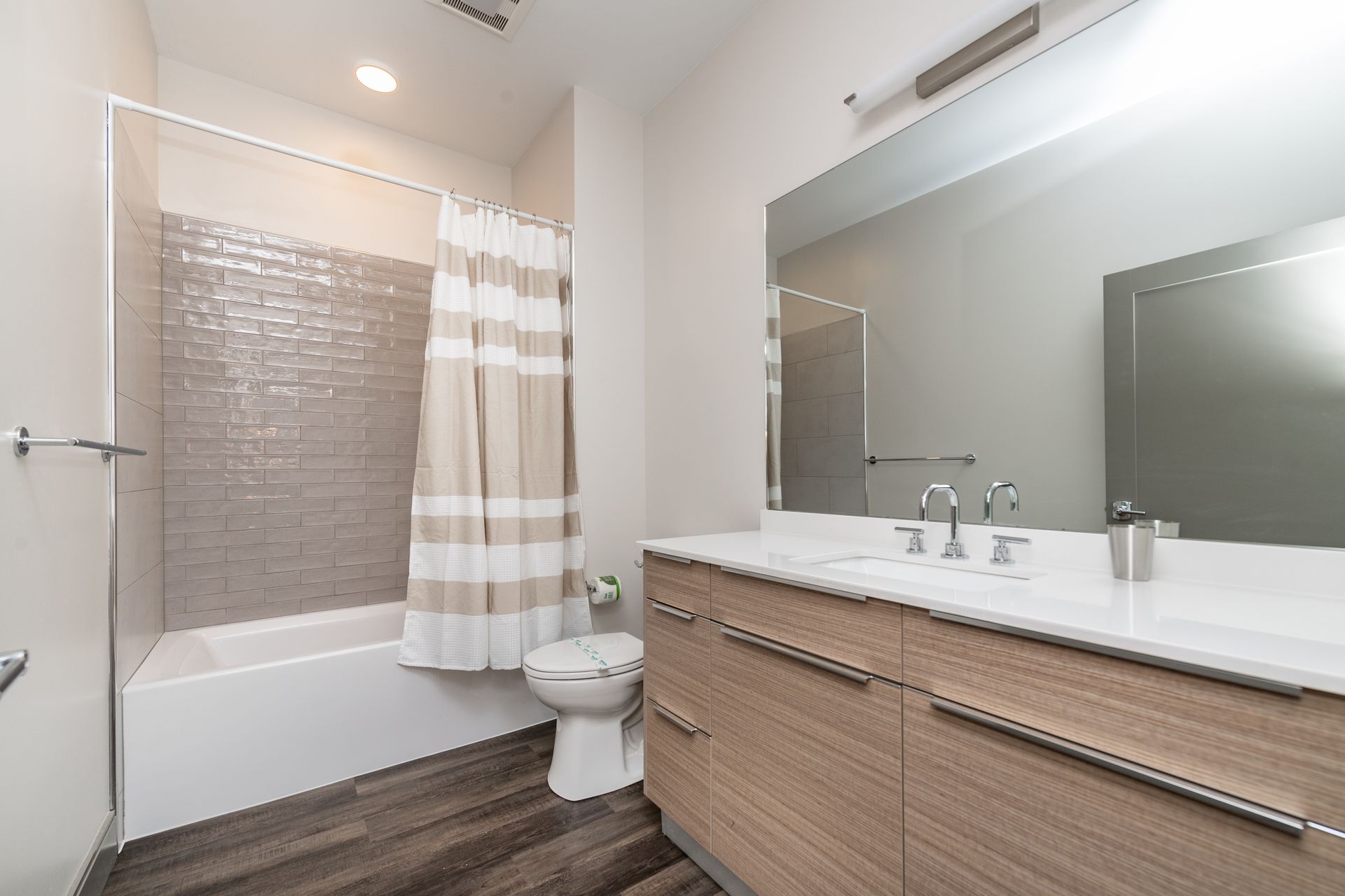 Bathroom with a white bathtub, toilet, vanity, large mirror, and shower curtain.