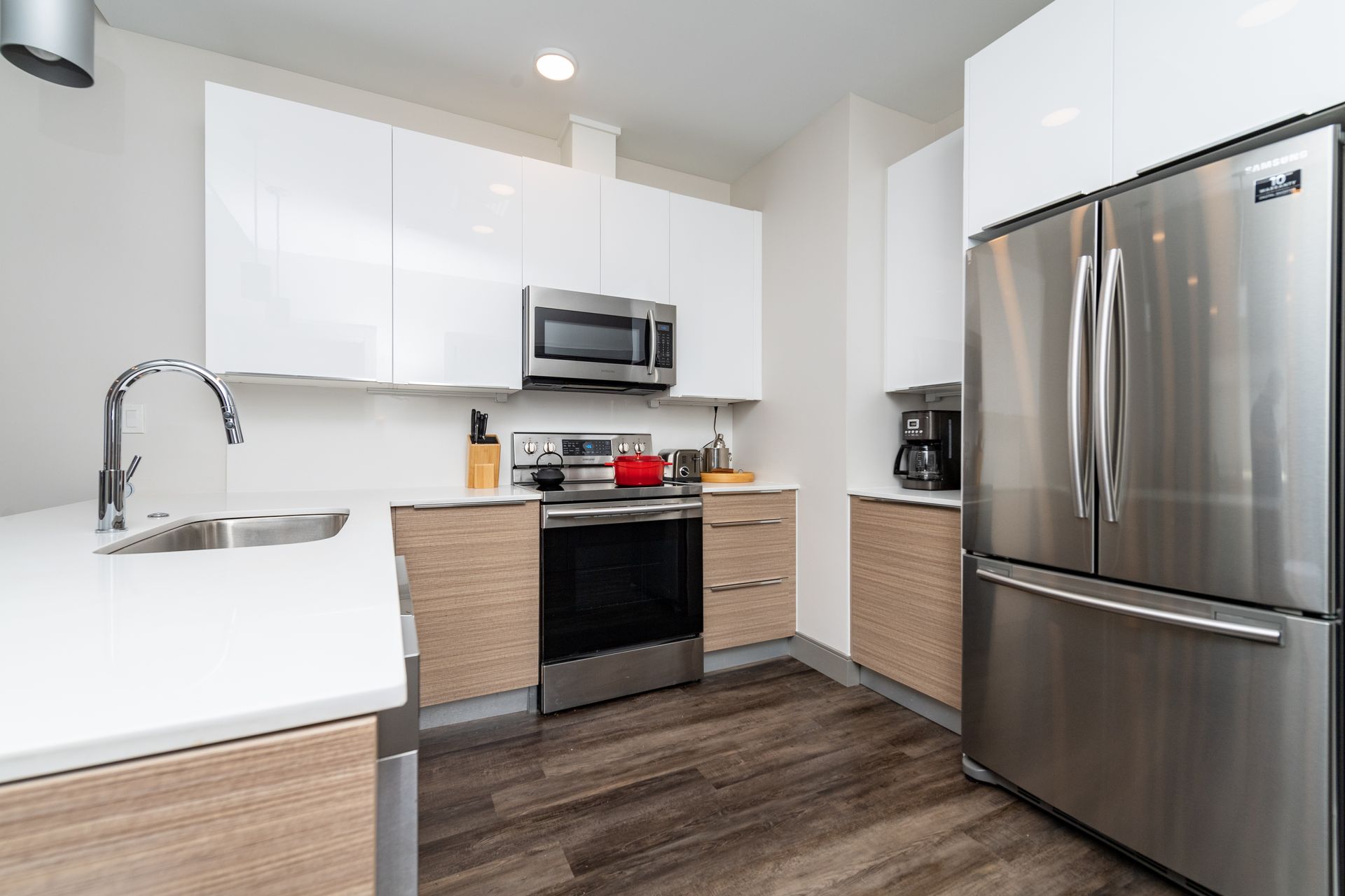 Modern kitchen with white and wood cabinets, stainless steel appliances, and dark wood flooring.