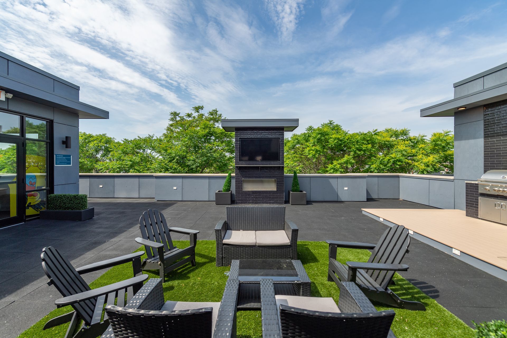 Rooftop patio with seating around a fire pit, outdoor fireplace, and green trees against a blue sky.