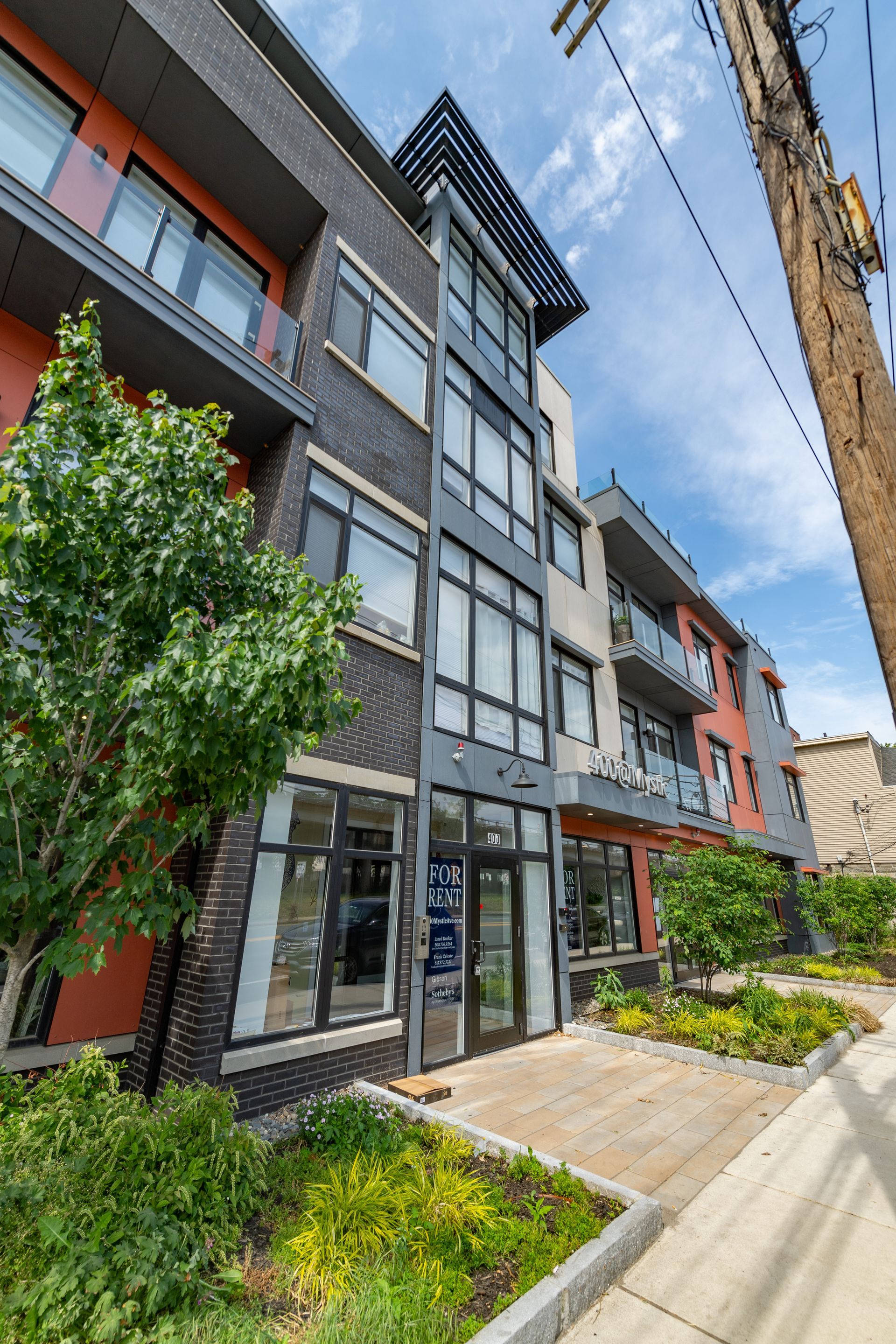 Modern multi-story building with balconies, brick and painted exterior, sunny day.