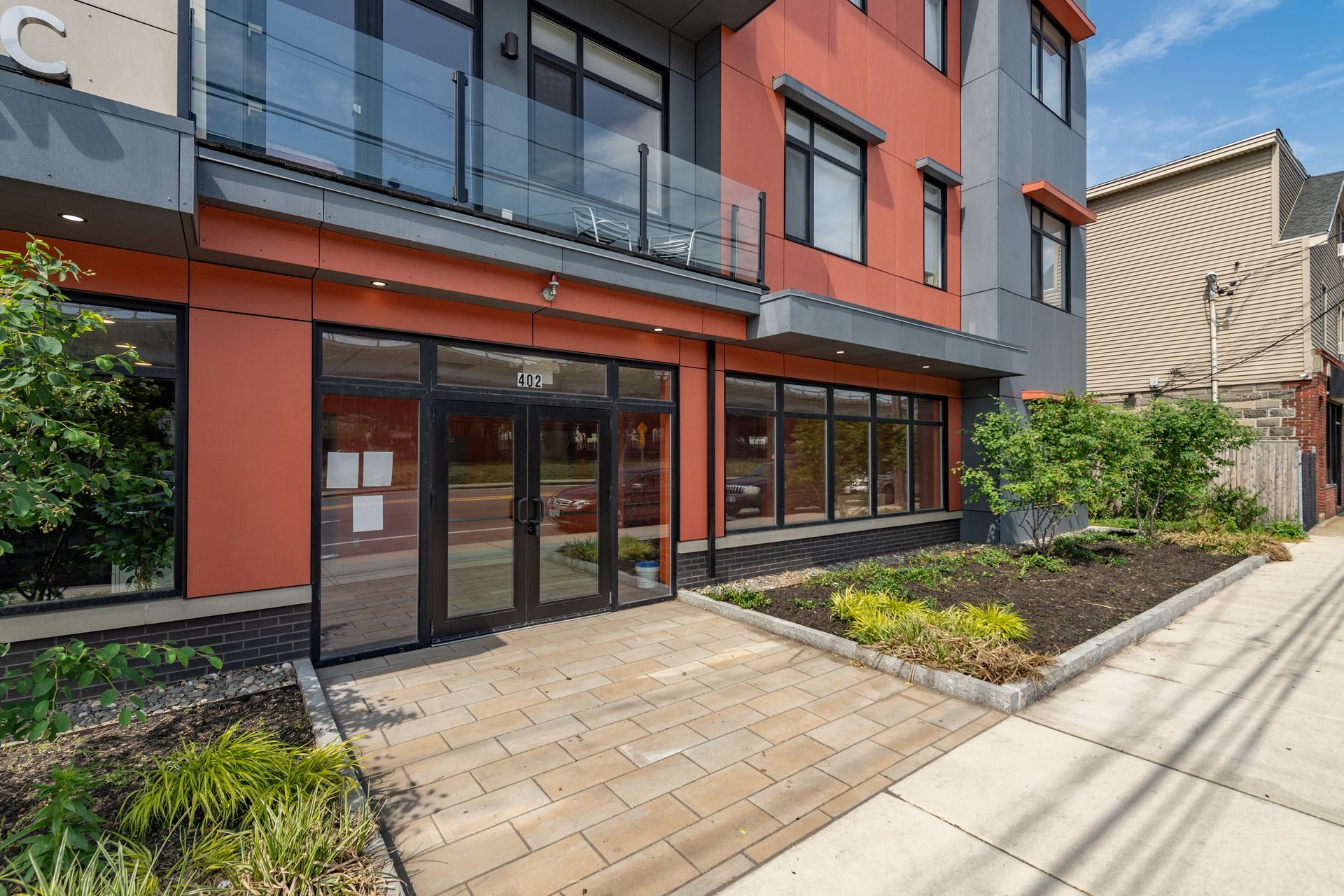 Modern building exterior with glass doors and windows, orange and gray facade, sidewalk.