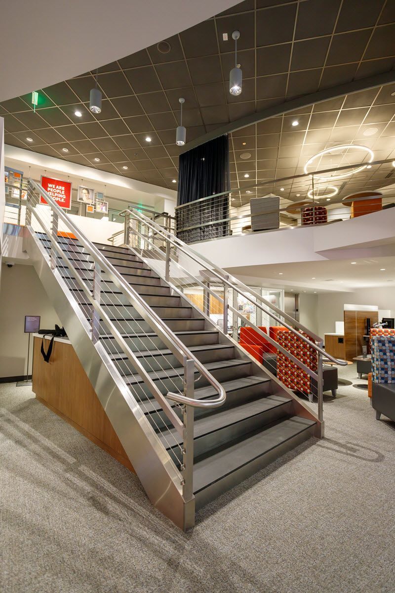 Staircase in a modern interior, featuring metal handrails, gray steps, and a view of a second floor.