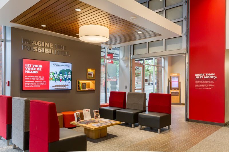 Modern lobby with red chairs, wall screens, and a small seating area under a hanging lamp