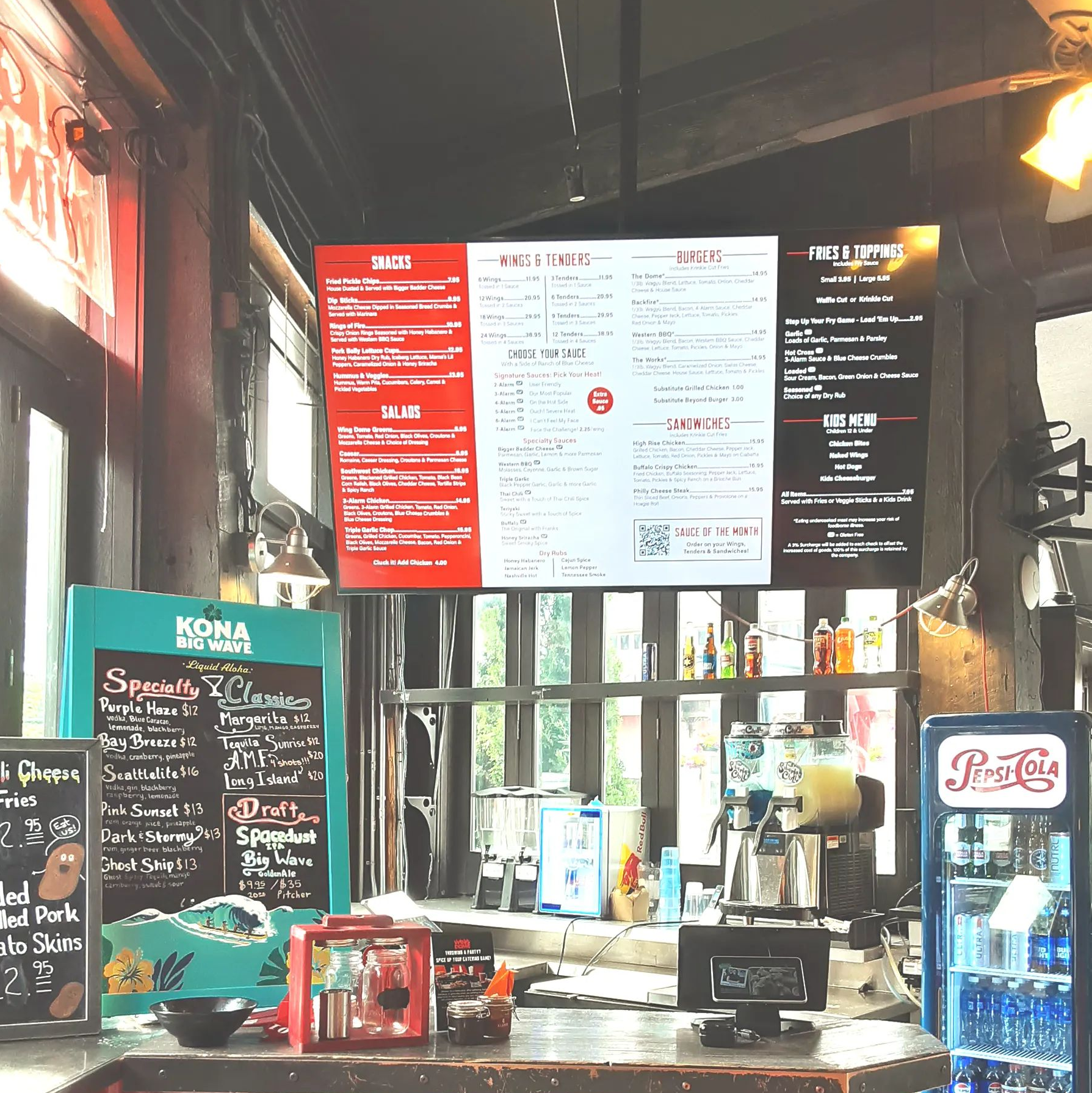 Coffee shop counter with large menu boards, chalkboard specials, and a drink cooler in a dim interior