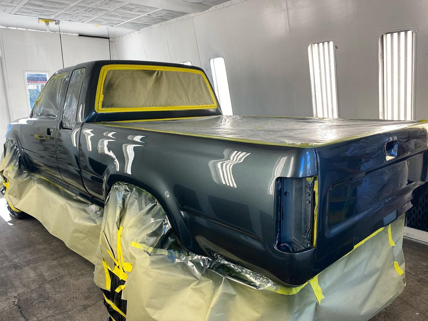 Pickup truck in paint booth, masked with yellow tape and plastic for repainting | Rev Limit Auto Center