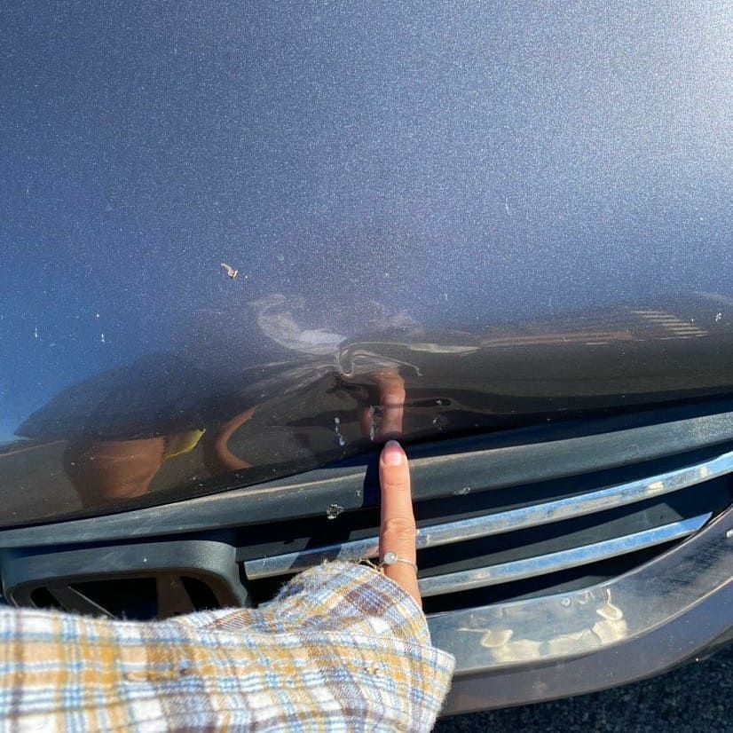 Finger pointing at a car hood above the front grille and bumper trim | Rev Limit Auto Center