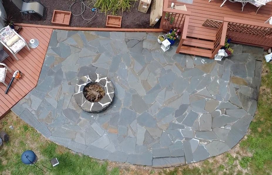 Overhead view of a stone patio with a fire pit, next to a wooden deck with steps.