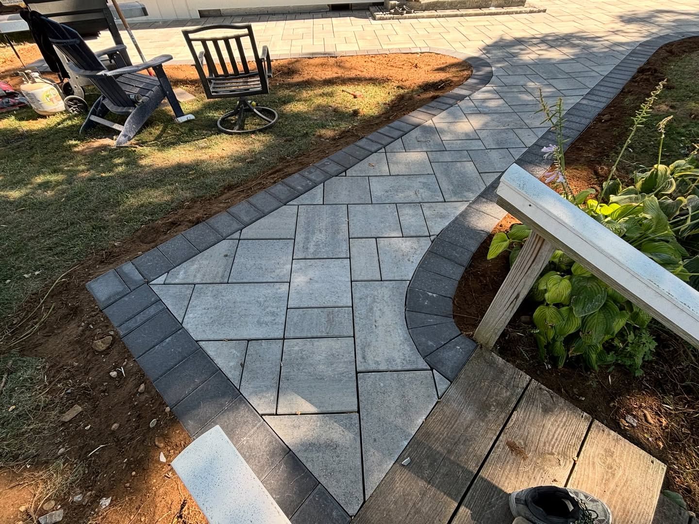 Paver walkway with dark border, gray stones, and curved edge near a deck.