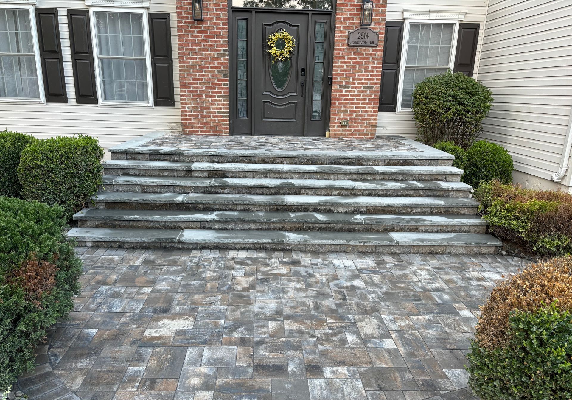 Stone steps and walkway leading to a house with brick facade, front door, and shrubs.