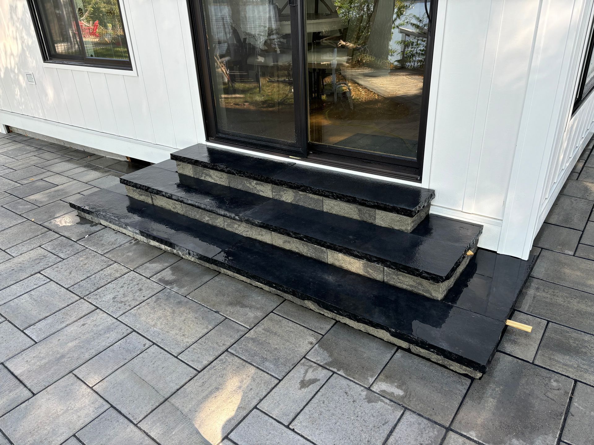 Black granite steps leading up to sliding glass doors, installed on a patio with gray pavers.