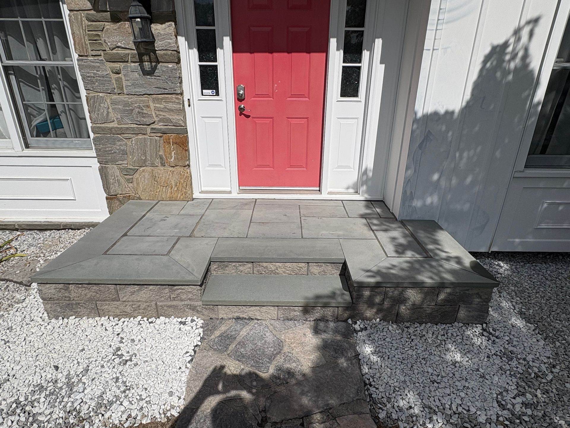 Stone front porch with red door. Pathway leads to a gray, rectangular step.
