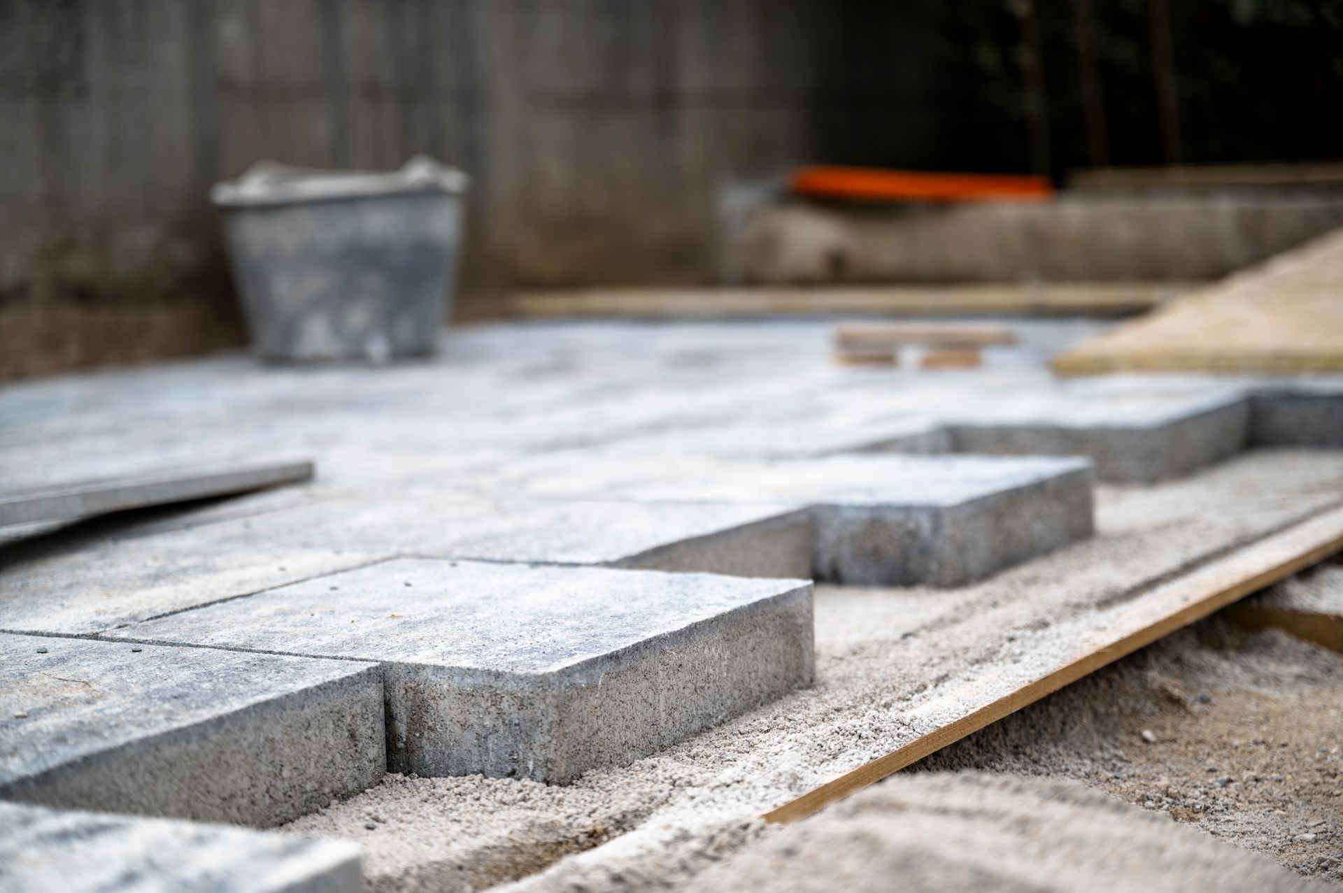Concrete pavers being installed on a patio, with a bucket and wooden planks nearby