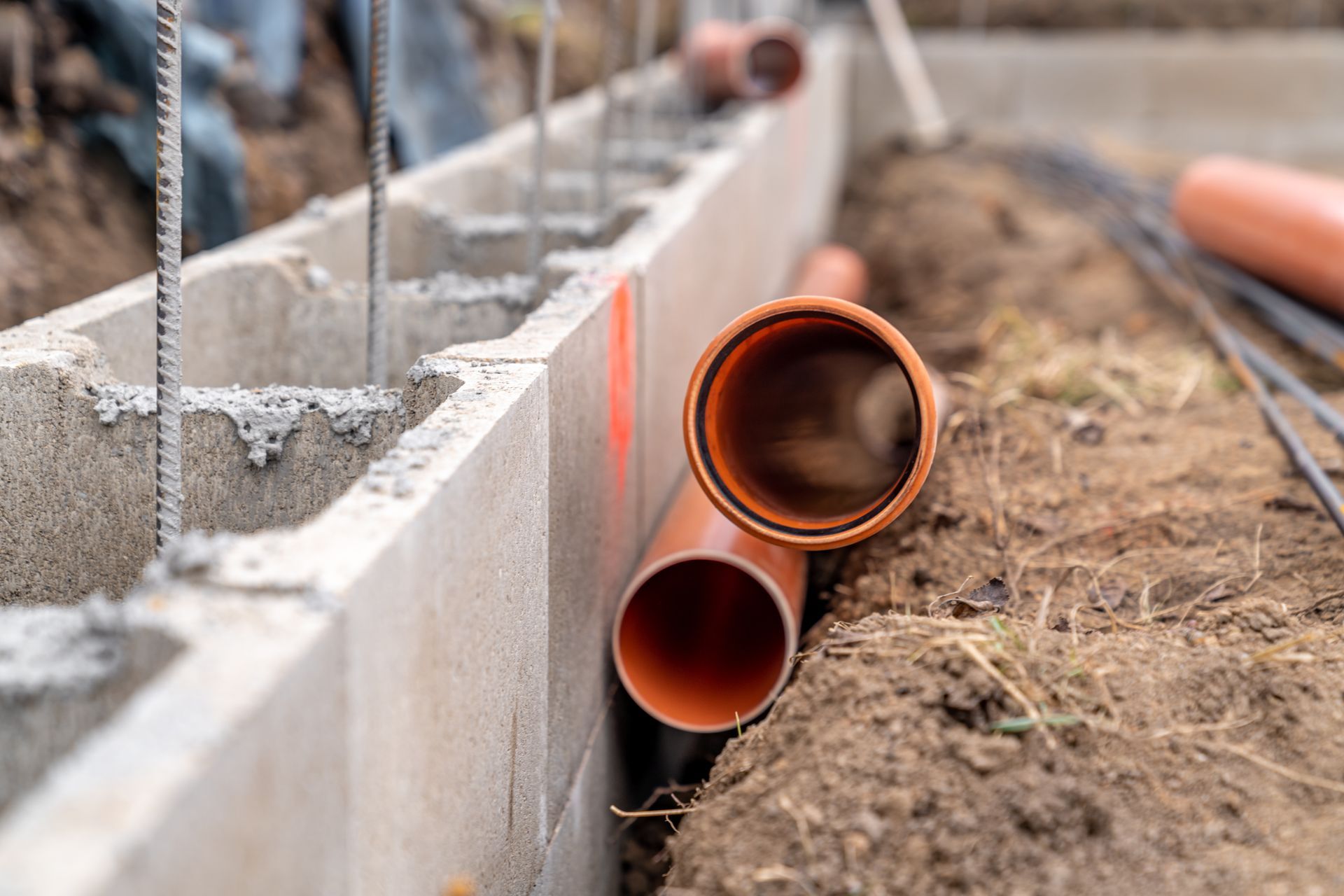 Orange drainage pipes beside a concrete foundation under construction