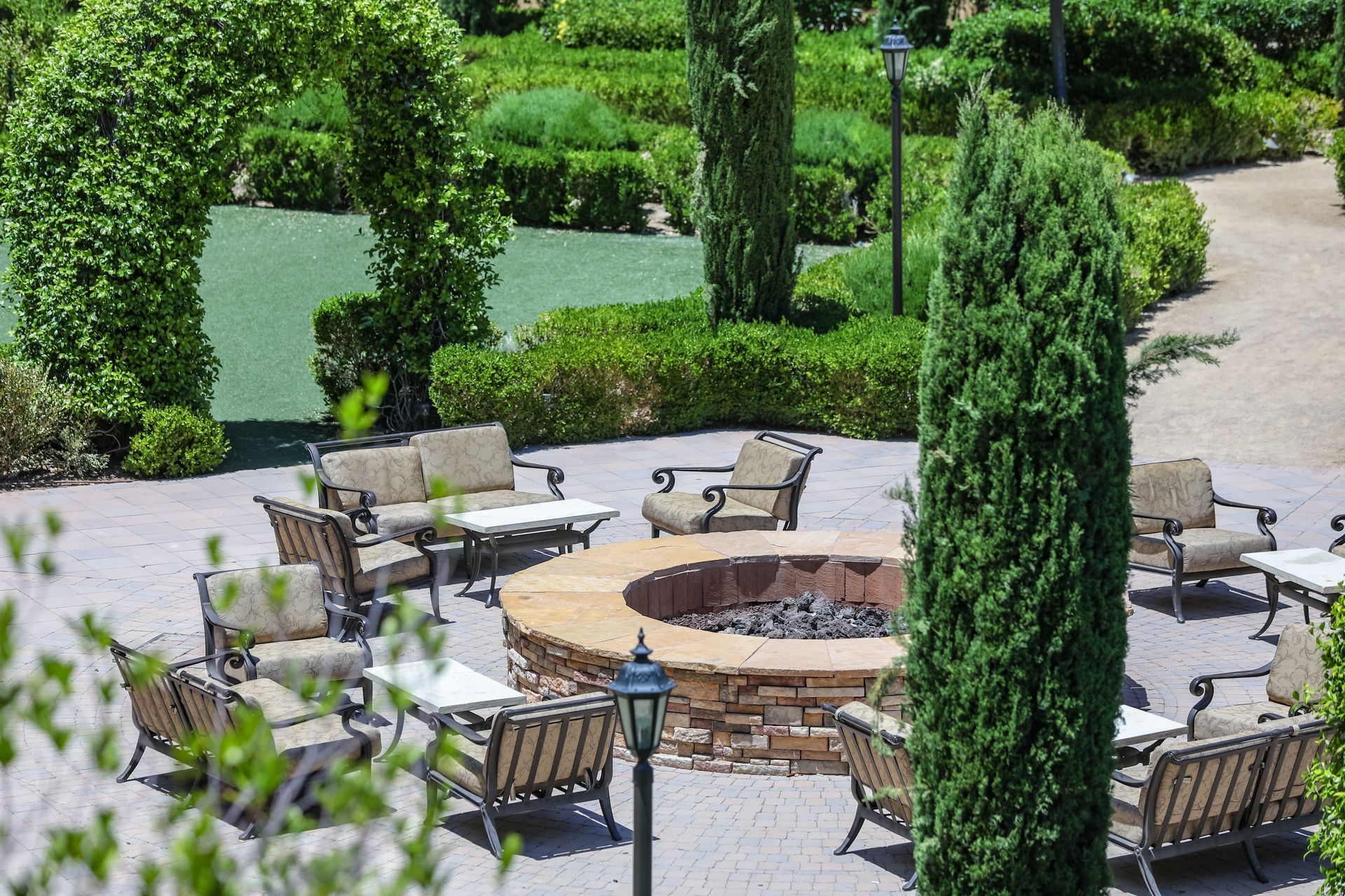 Patio seating around a stone fire pit in a landscaped garden with hedges and trees