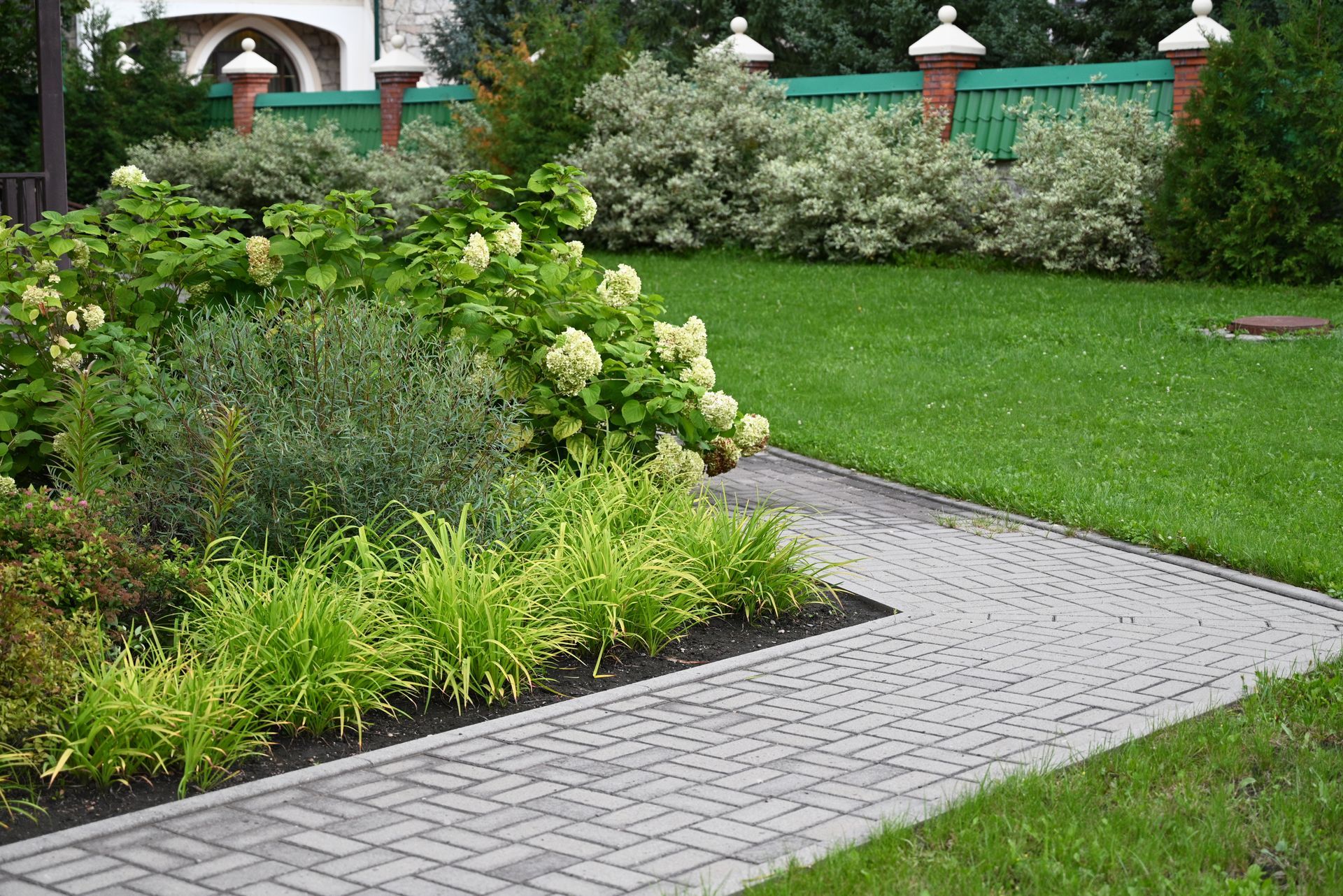 Curved stone garden path beside lush green shrubs and white flowers in a landscaped yard