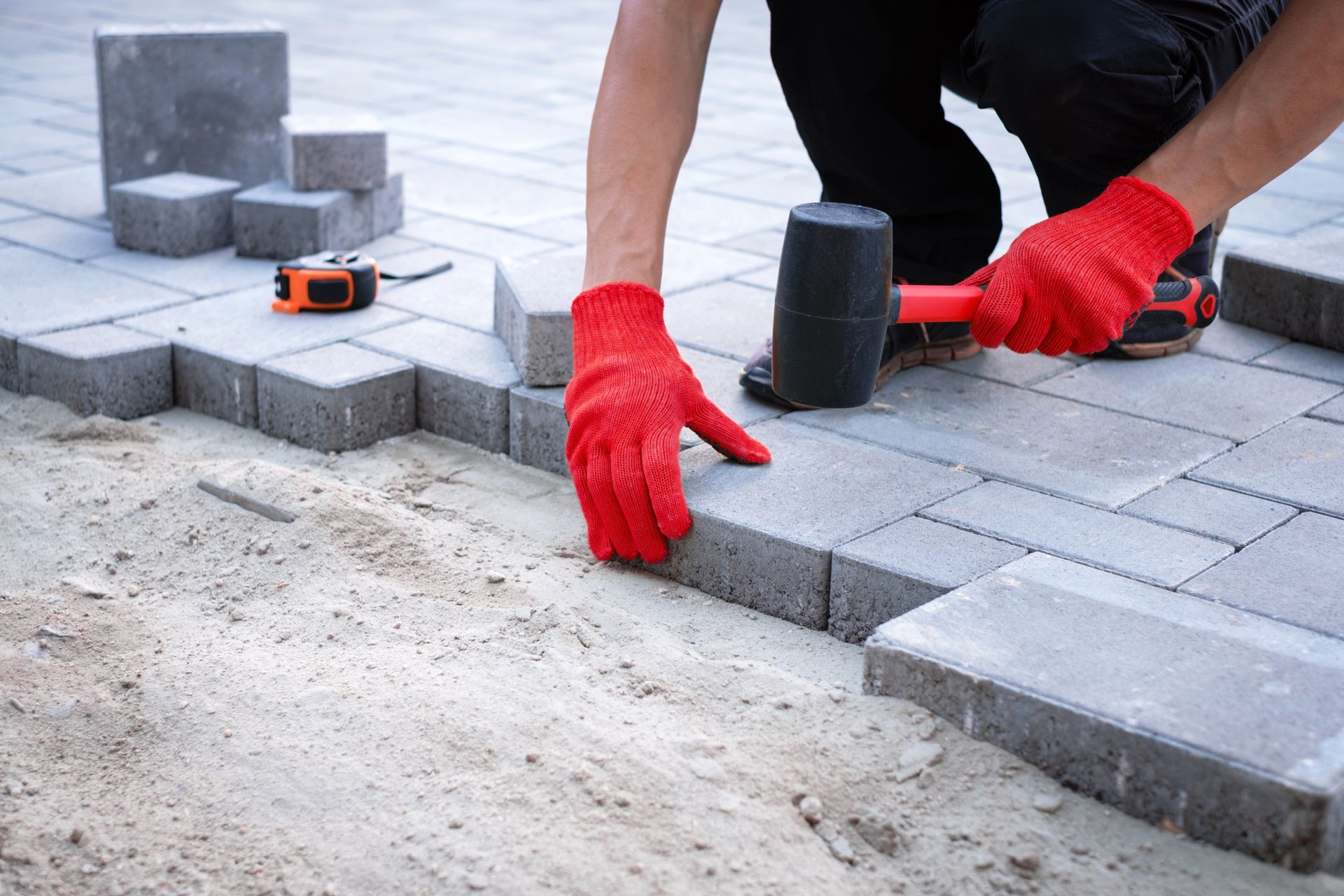 Worker laying gray paving stones with red gloves and a rubber mallet outdoors