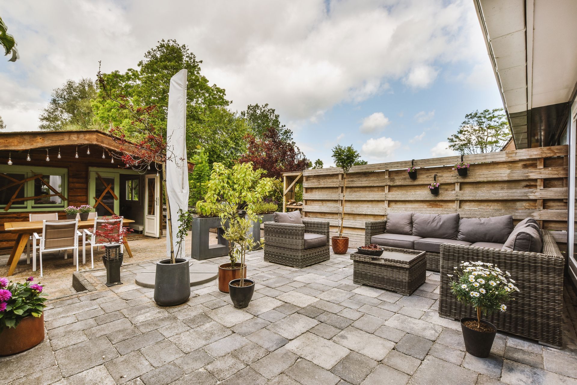 Patio with wicker seating, potted plants, fire pit, and a wooden pergola under a cloudy sky