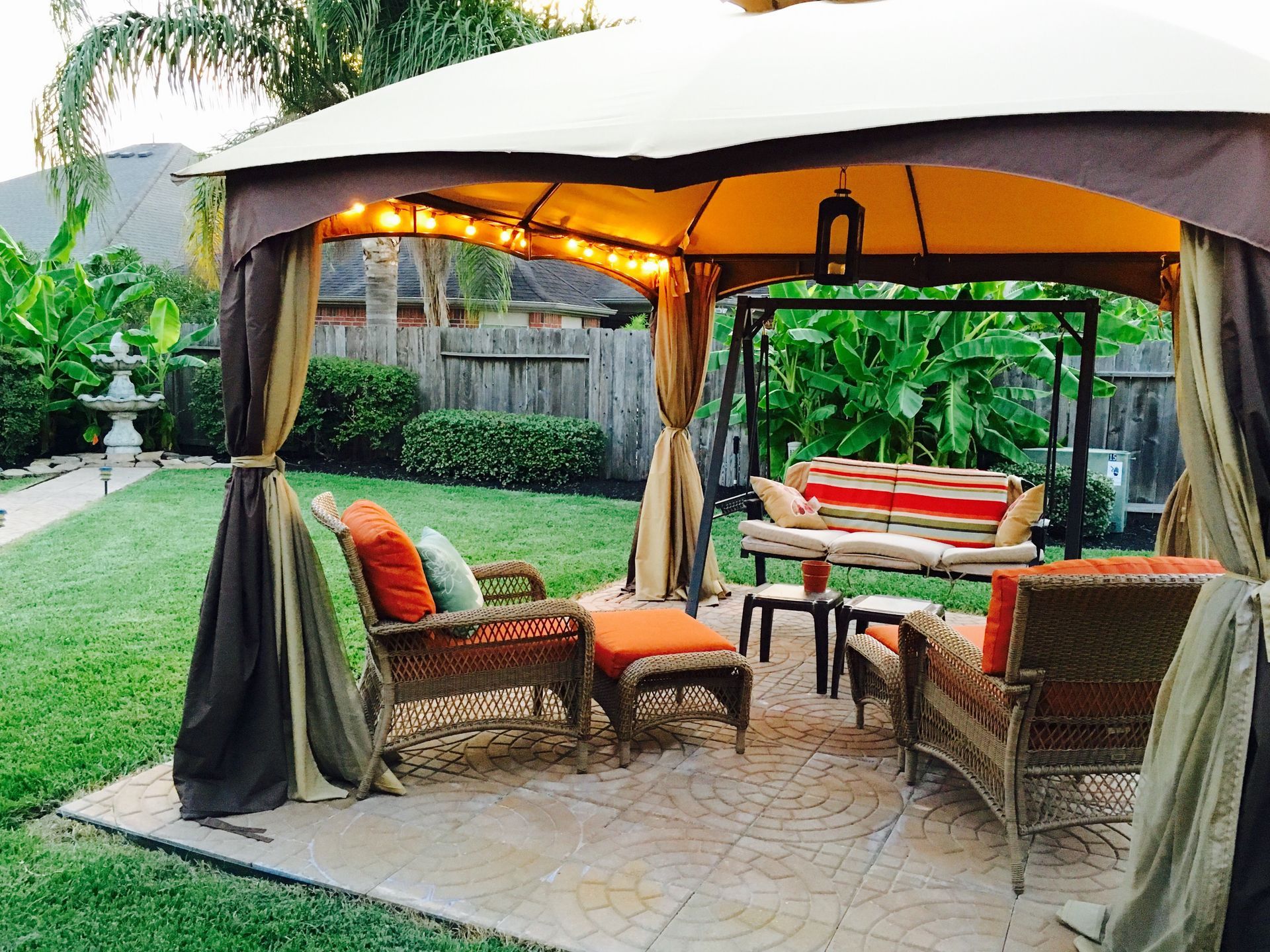 Covered patio seating area with wicker chairs, striped cushions, and warm garden lighting
