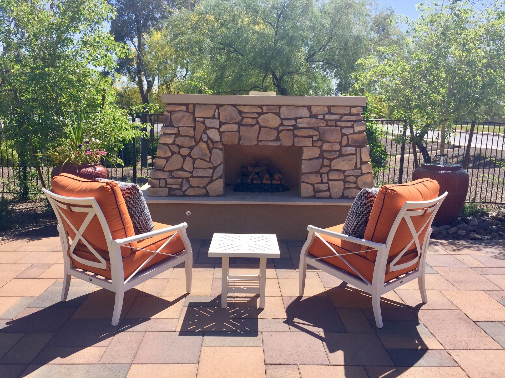 Patio seating around a stone outdoor fireplace with orange-cushioned chairs and a small table