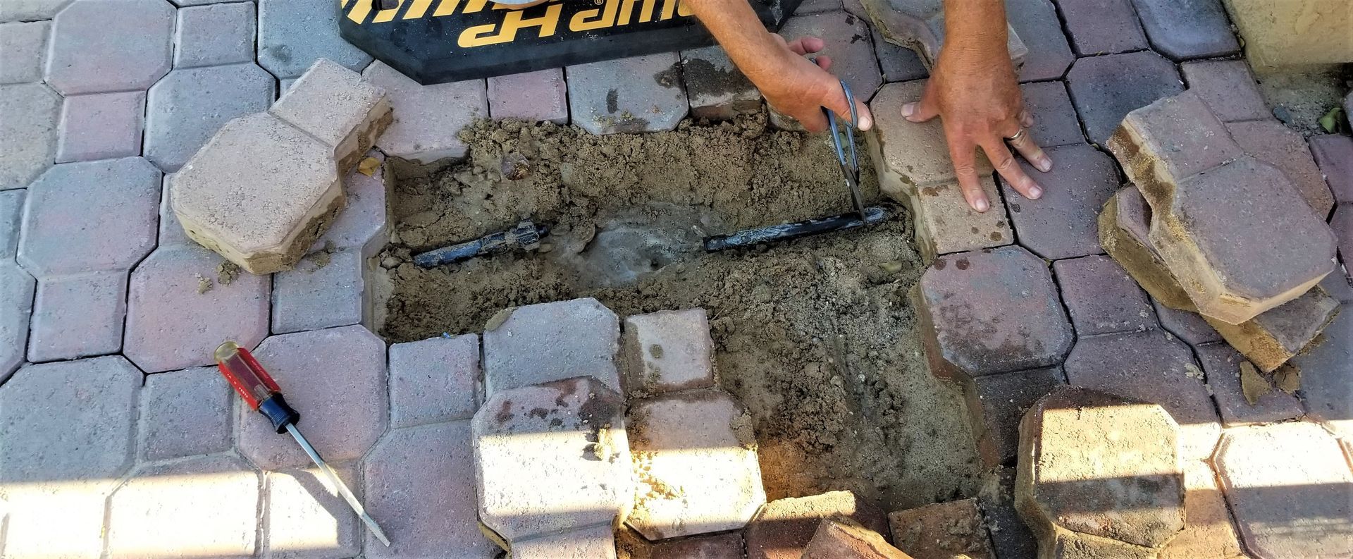 Hands laying concrete pavers around a wet cement patch on a brick walkway