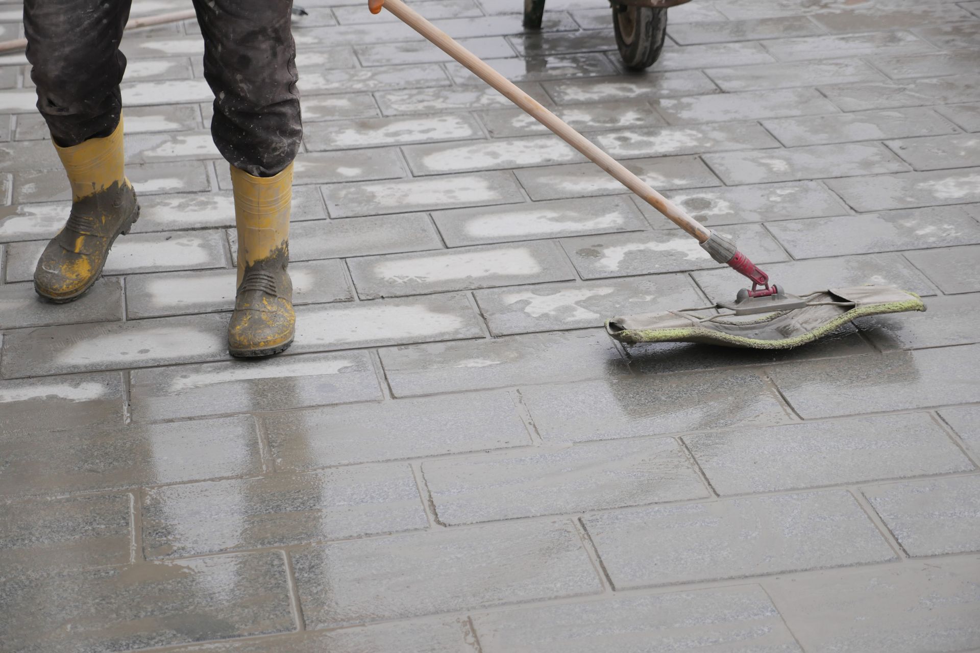 Worker sweeping wet pavement with a mop beside another person’s boots